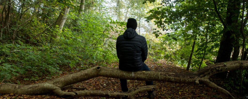 Person sitting quietly in nature, looking thoughtful and reflective
